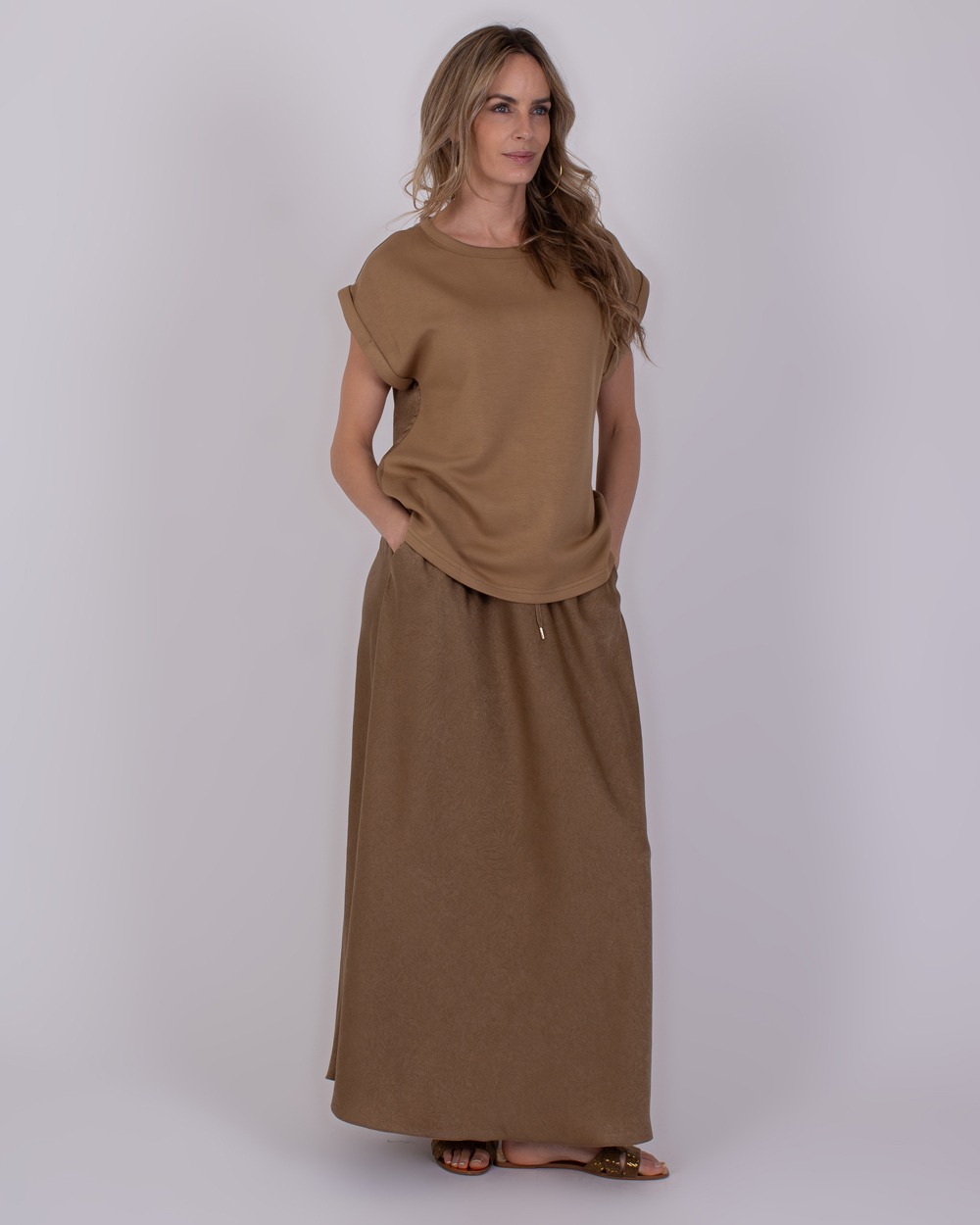 Troje taupe 1 Vrouw draagt een taupekleurige Troje-set met losvallende top en lange rok.