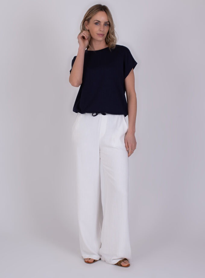 Vrouw draagt een donkerblauw Umea Navy 3 T-shirt met losse witte broek en sandalen.