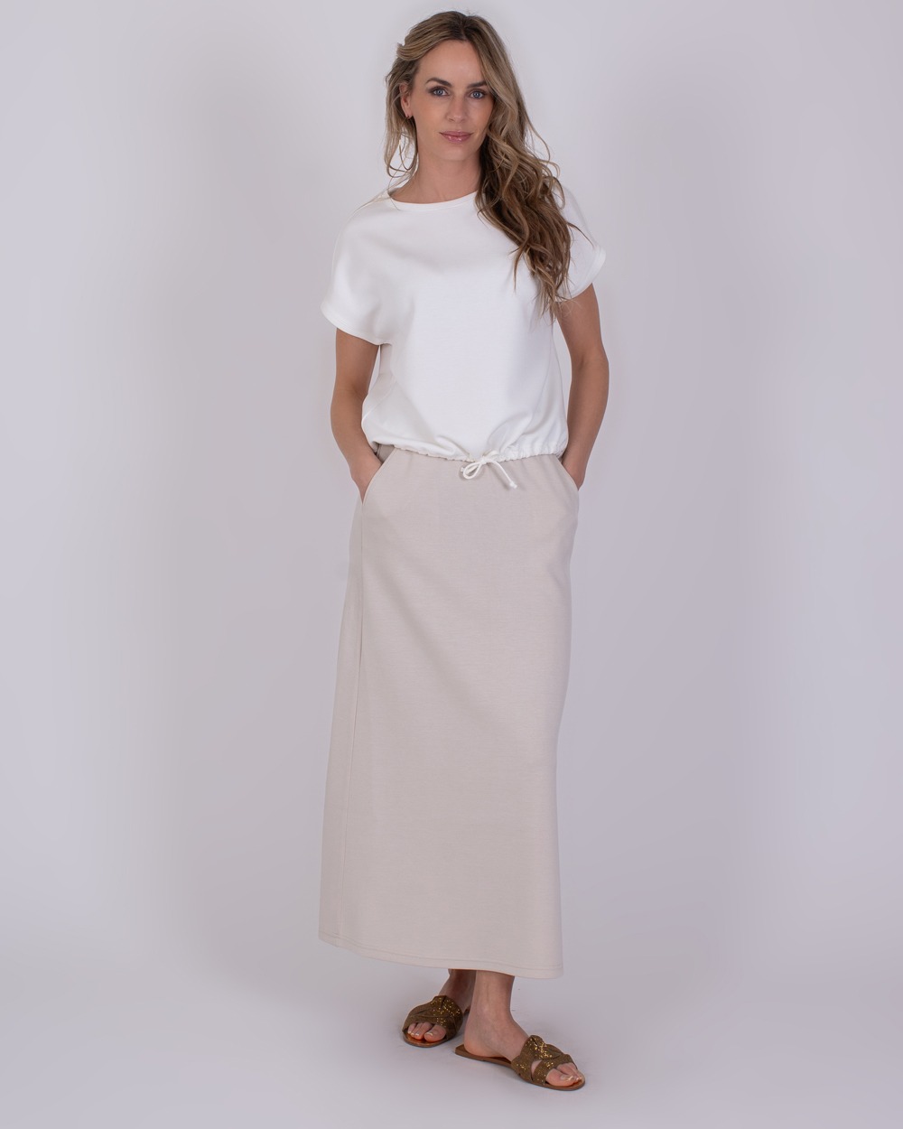Umea off white 1 Vrouw draagt een offwhite Umea-set bestaande uit een losvallend T-shirt en een lange rok met trekkoord.