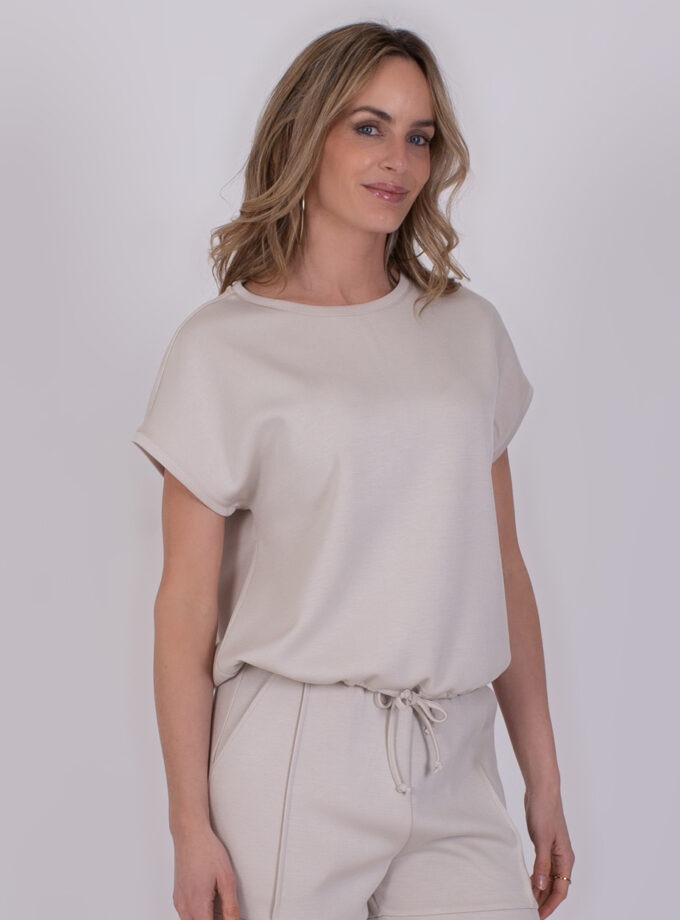 Vrouw draagt een comfortabele, lichtbeige Umea Pale 2 lounge-outfit met korte mouwen en trekkoord in de taille.