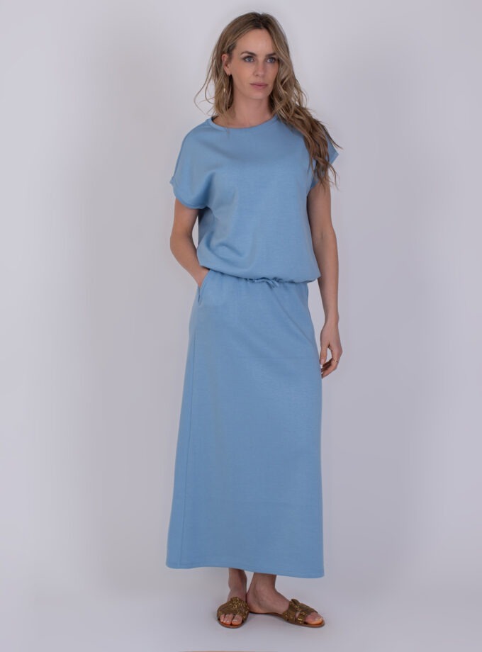 Vrouw draagt een lichtblauwe Umea-jurk met korte mouwen en een lange rechte rok.