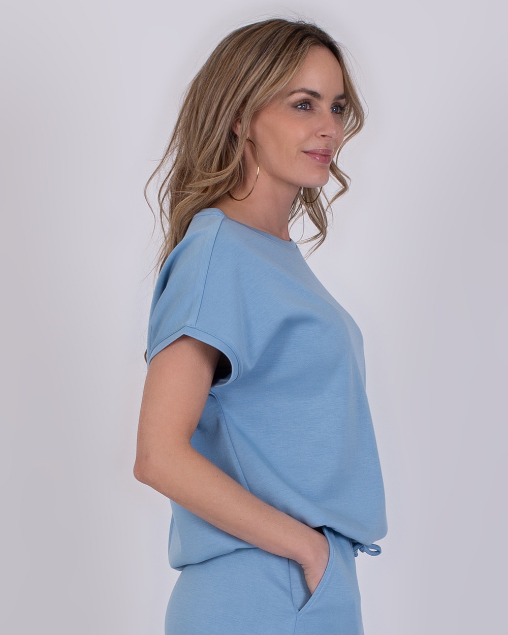 Umea soft blue 4 Vrouw in zijaanzicht draagt een lichtblauwe Umea soft blue outfit met korte mouwen.