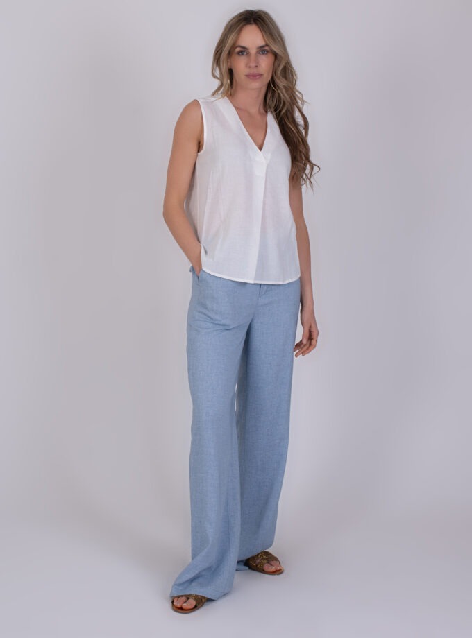 Vrouw draagt een mouwloze off-white Valdris-top met een V-hals, gecombineerd met lichtblauwe wijde broek.