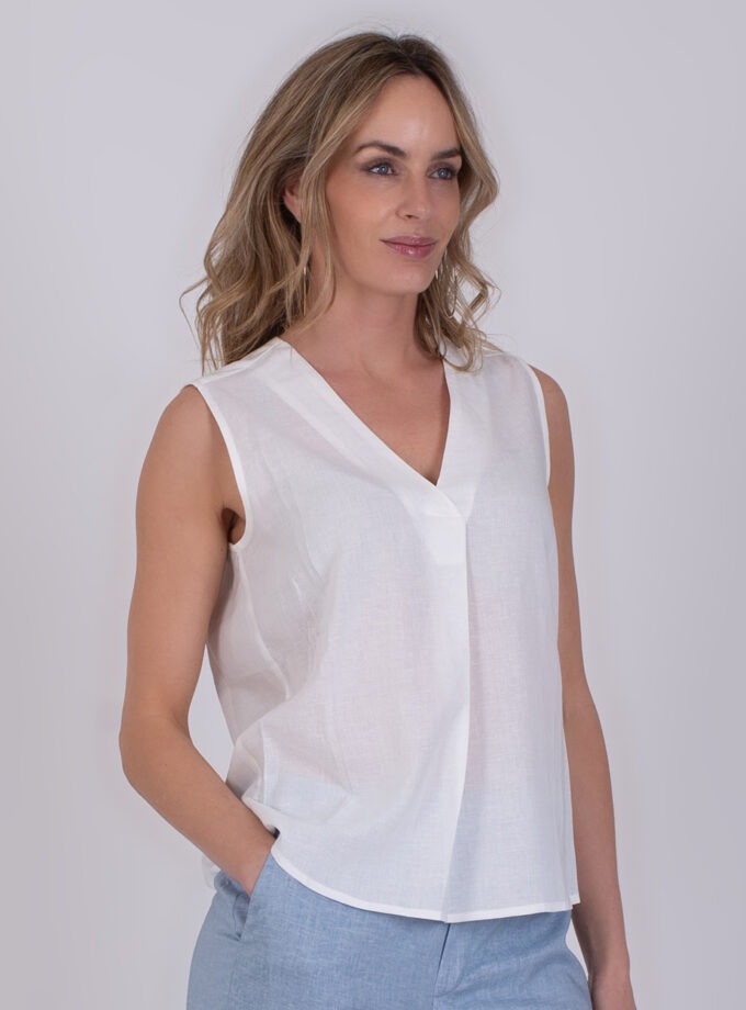 Vrouw draagt een mouwloze witte Valdris top met V-hals en lichtblauwe broek.