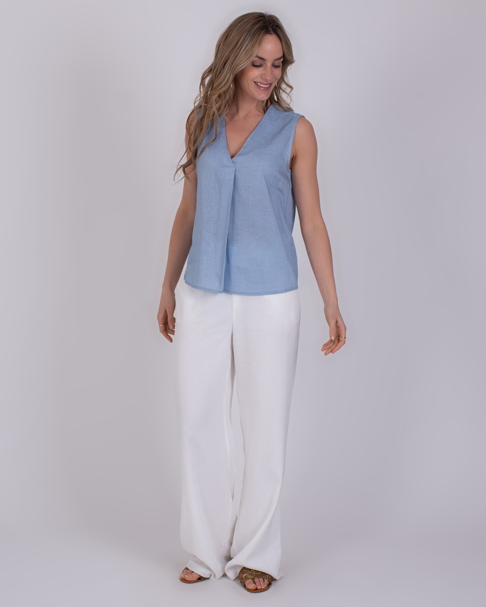 Valdris soft blue 1 Vrouw draagt een mouwloze Valdris top in lichtblauw met een V-hals, gecombineerd met witte, wijde broek.