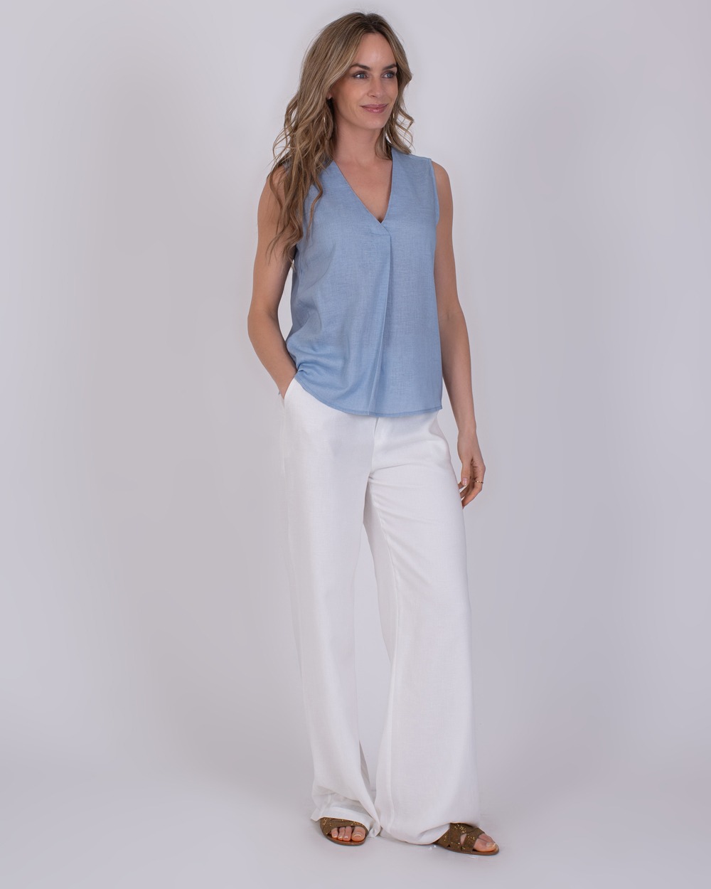 Valdris soft blue 2 Vrouw draagt een mouwloze Valdris soft blue top met V-hals en witte, wijde broek.