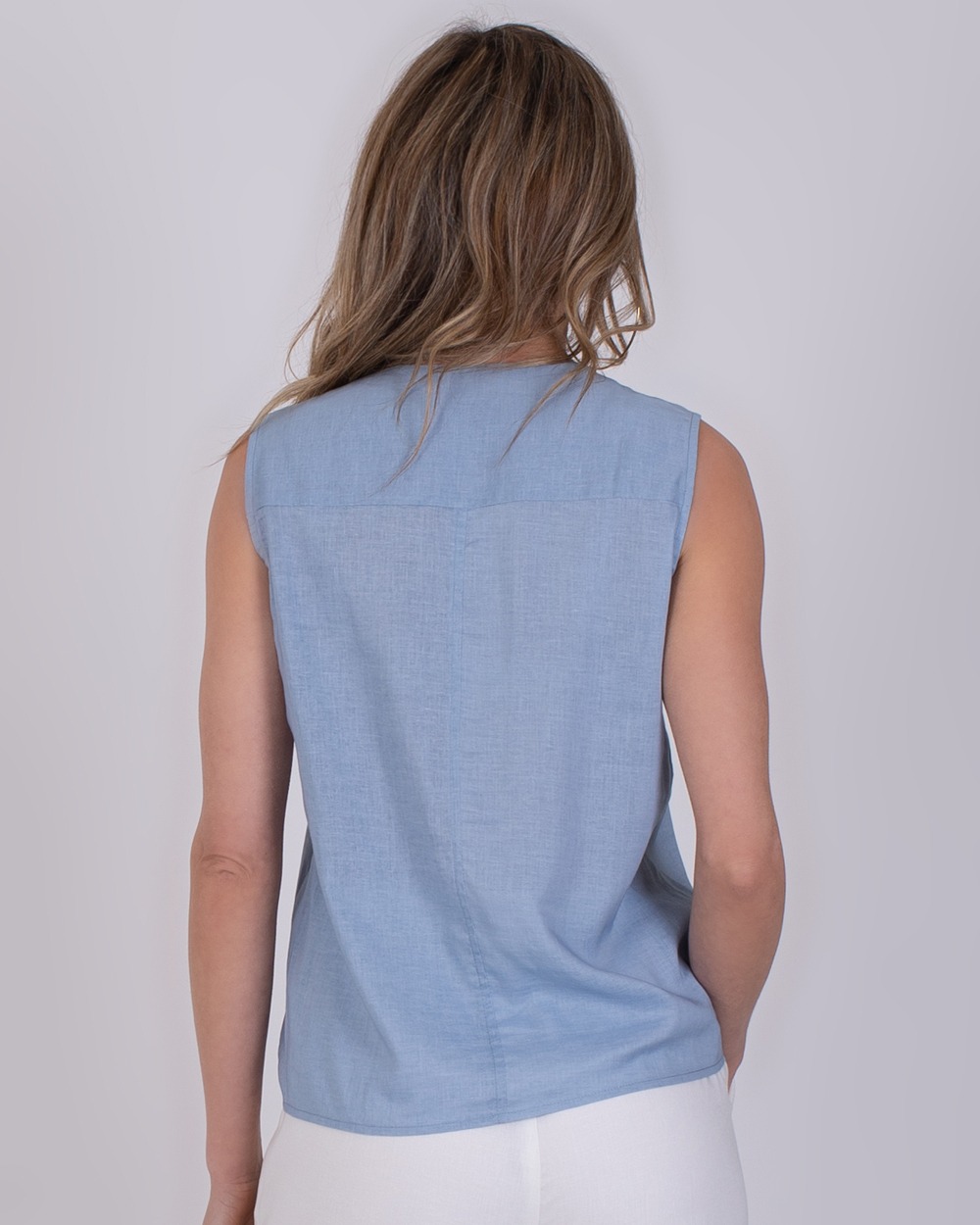 Valdris soft blue 4 Vrouw van achteren in een mouwloze, lichtblauwe Valdris-top en witte broek.