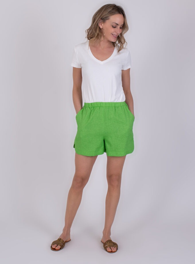 Vrouw draagt een witte T-shirt en felgroene Varenna Sea Green short met haar handen in de zakken.
