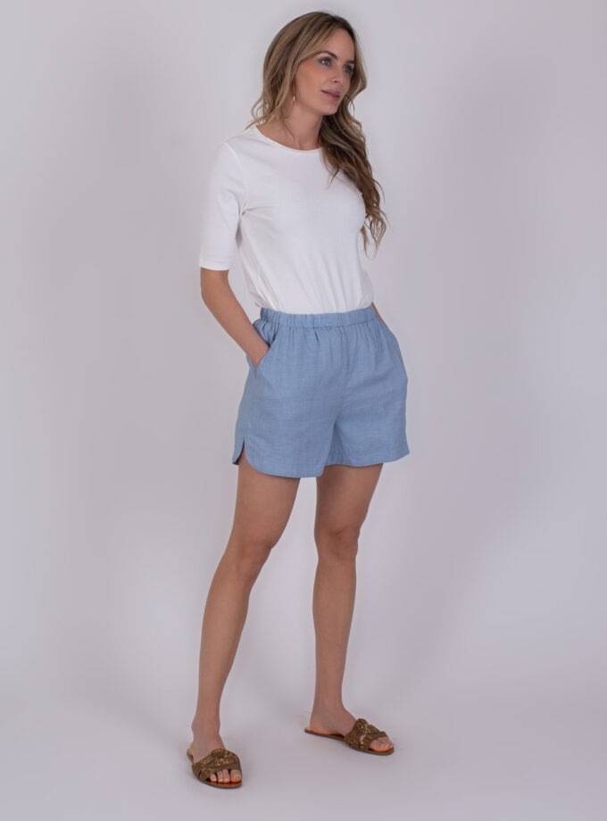 Vrouw draagt een witte top en lichtblauwe Varenna soft blue shorts met elastische taille en splitjes aan de zijkant.