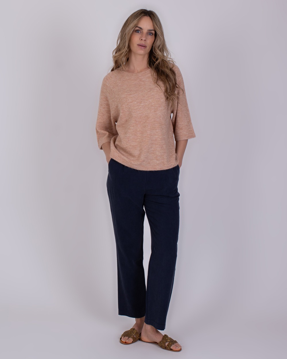 Vrouw draagt een losse, oudroze Volos-trui met driekwartsmouwen en donkerblauwe broek.