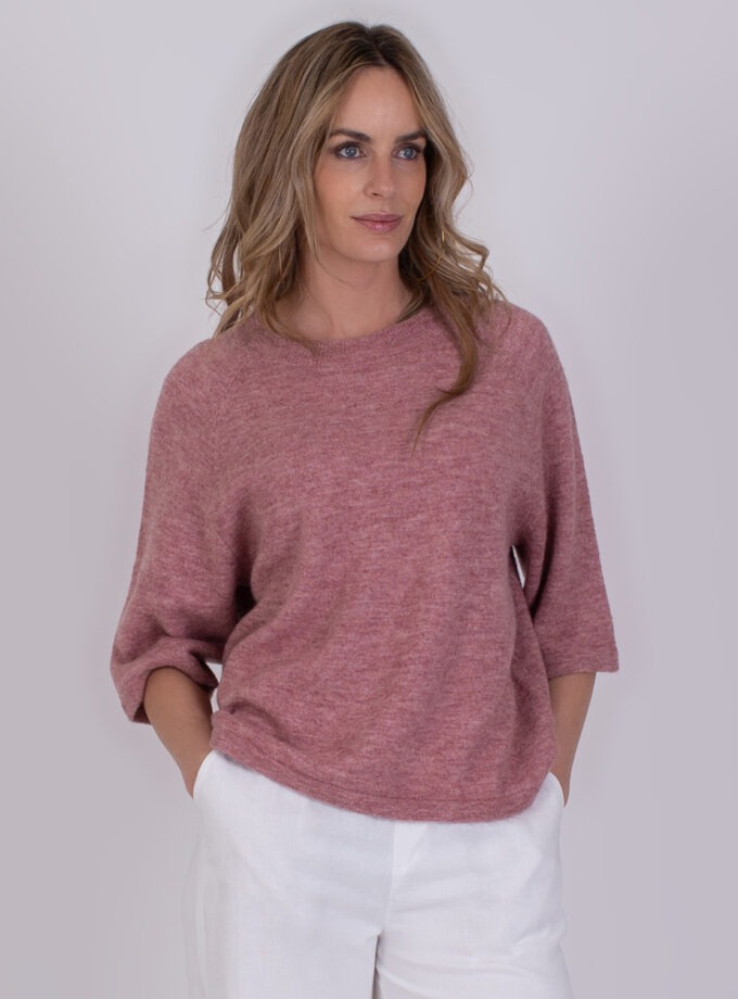 Vrouw draagt een Volos-trui in frambozenroze met driekwartmouwen en witte broek.