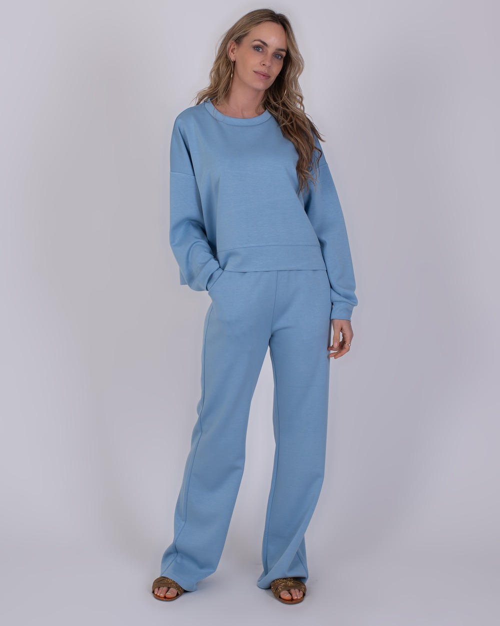 York soft blue 1 Vrouw draagt een comfortabele, lichtblauwe York soft blue set bestaande uit een sweatshirt en wijde broek.