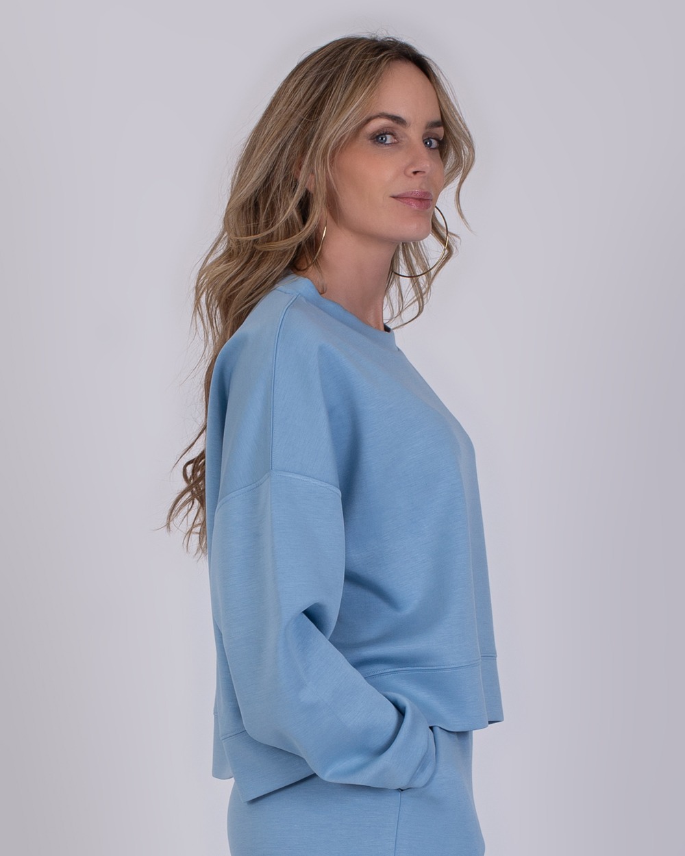 York soft blue 2 Vrouw in zijaanzicht draagt een lichtblauwe York soft blue trui met bijpassende broek.