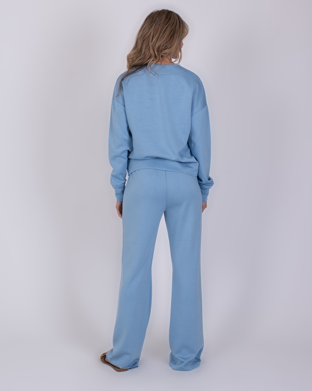 York soft blue 7 Vrouw van achteren in een lichtblauw York Soft Blue 7 loungepak met lange mouwen en wijde broekspijpen.