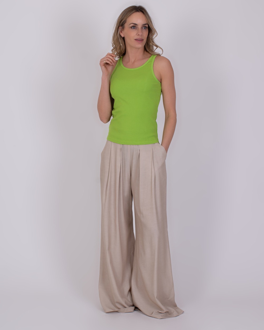 Ypres lime 2 Vrouw draagt een limegroene Ypres-top met beige, wijde plooibroek tegen een neutrale achtergrond.