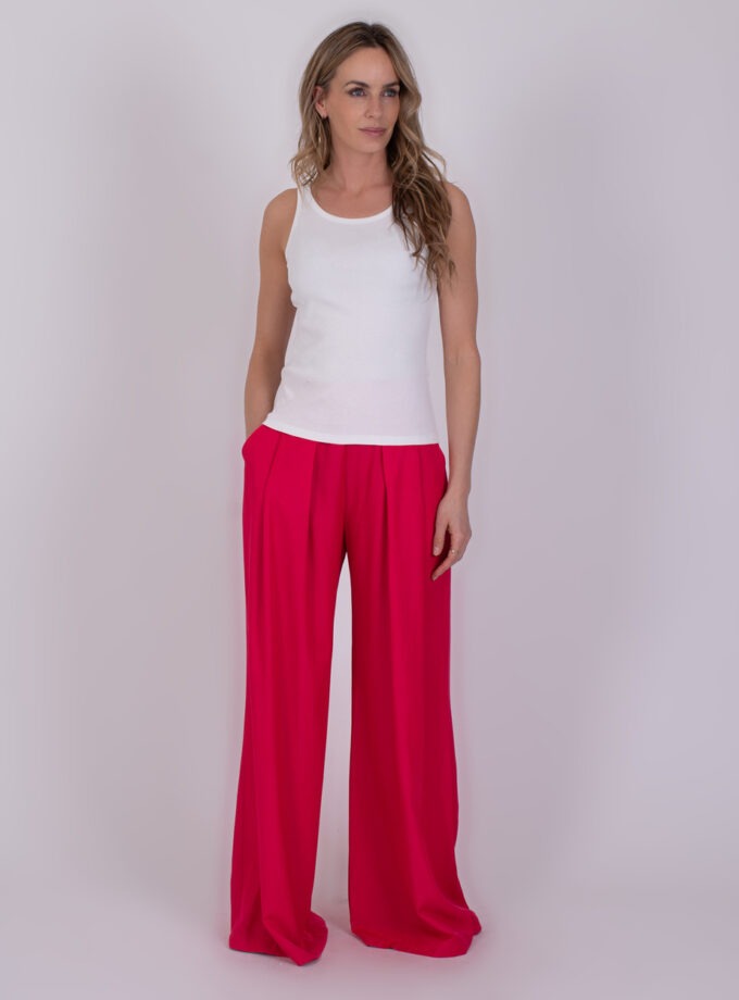 Vrouw draagt een offwhite Ypres-top met felroze, wijde broek tegen een neutrale achtergrond.