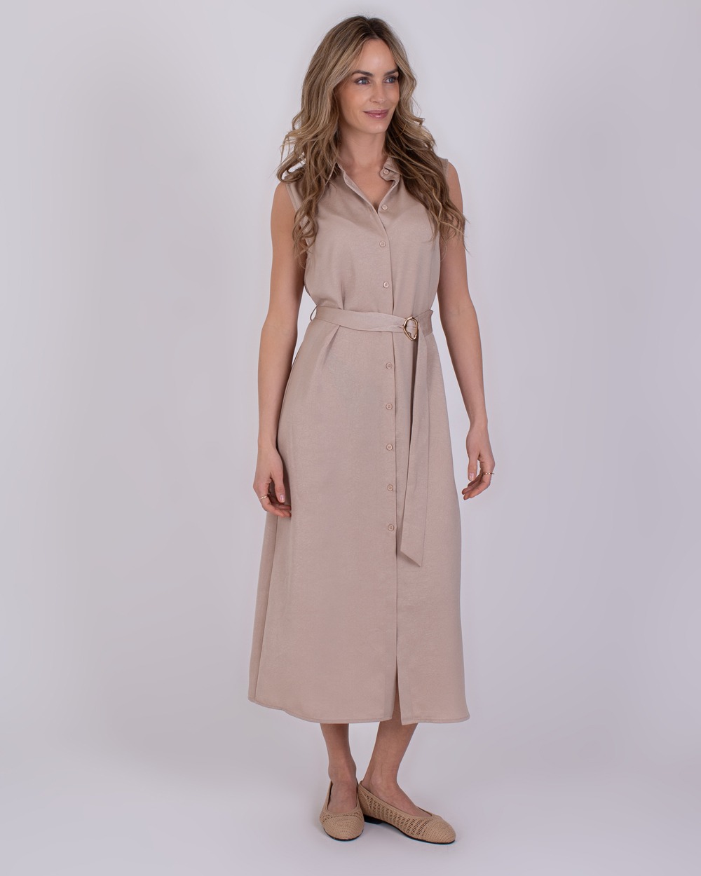 Zaria pale 2 Vrouw draagt een mouwloze, lichtbeige Zaria-jurk met knopen en een ceintuur.