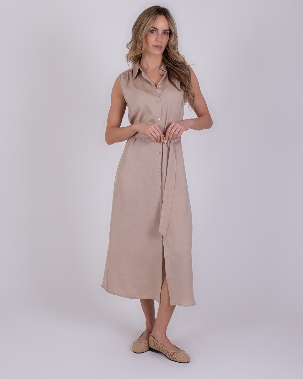Zaria pale 3 Vrouw poseert in een mouwloze, lichtbeige Zaria Pale 3 doorknoopjurk met ceintuur.