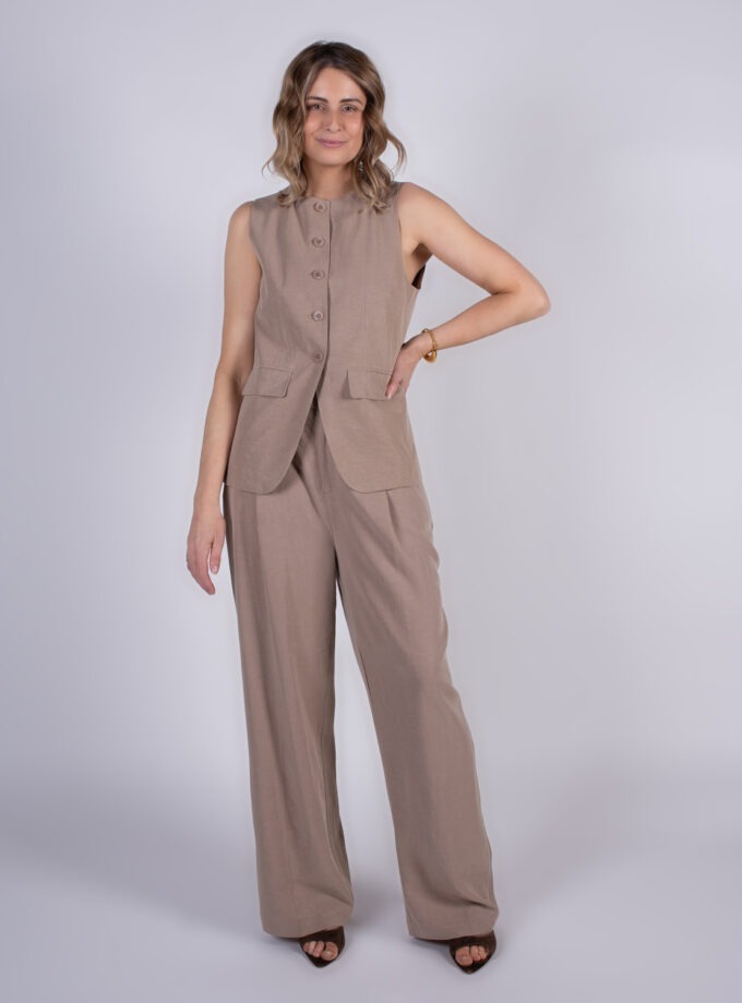 Een model poseert in een beige mouwloos vest en bijpassende broek tegen een neutrale achtergrond.