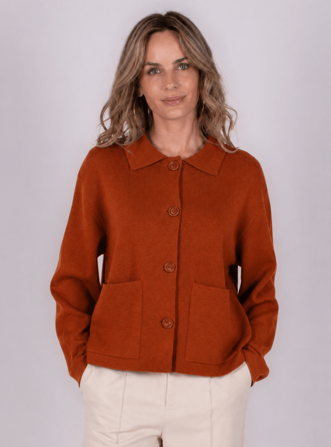 Een vrouw draagt een kaneelkleurige Alta cardigan met knopen en zakken, gefotografeerd tegen een grijze achtergrond.