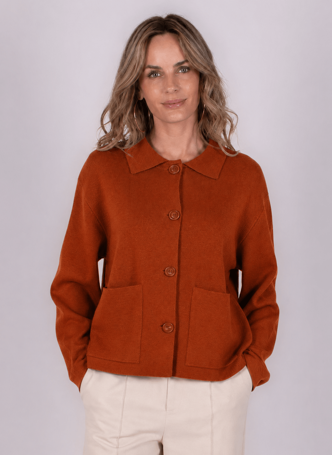 Een vrouw draagt een kaneelkleurige Alta cardigan met knopen en zakken, gefotografeerd tegen een grijze achtergrond.
