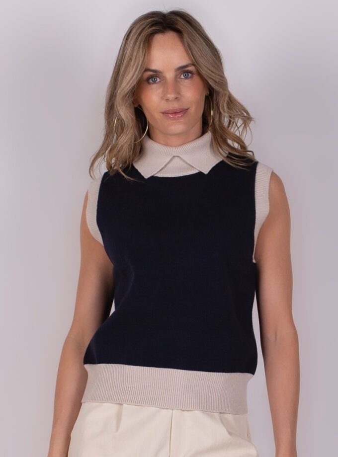 Een vrouw draagt een navy mouwloze Arhus Spencer met een beige kraag en boorden, gefotografeerd vanuit een frontale hoek.