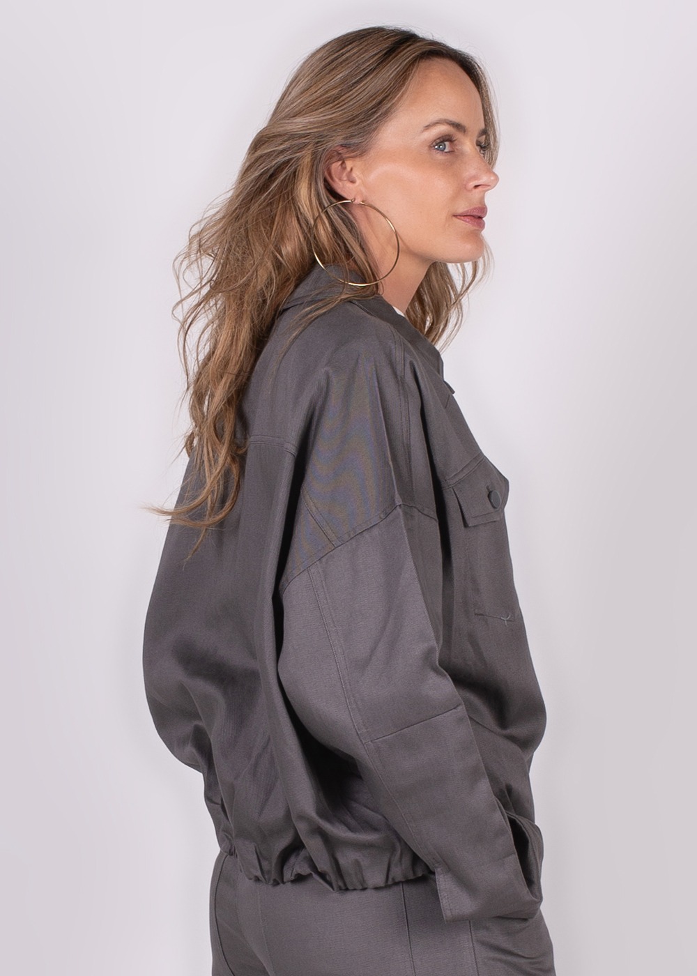 Een vrouw met lang haar draagt een grijze Balam-jack, gezien van de zijkant met een neutrale achtergrond.