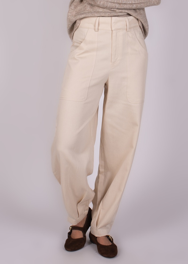 Beige, wijde broek genaamd "Balam pant-118" gedragen met bruine schoenen en een gedrapeerde trui, vanuit een hoek recht van voren.
