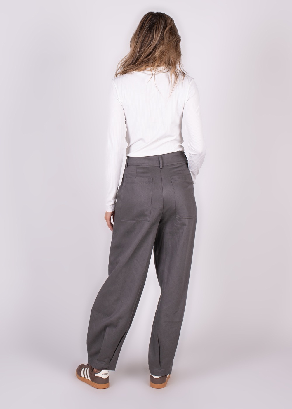 Een persoon in een witte top en grijze Balam-pant is vanaf de achterkant gefotografeerd, waarbij de focus op de broek ligt.