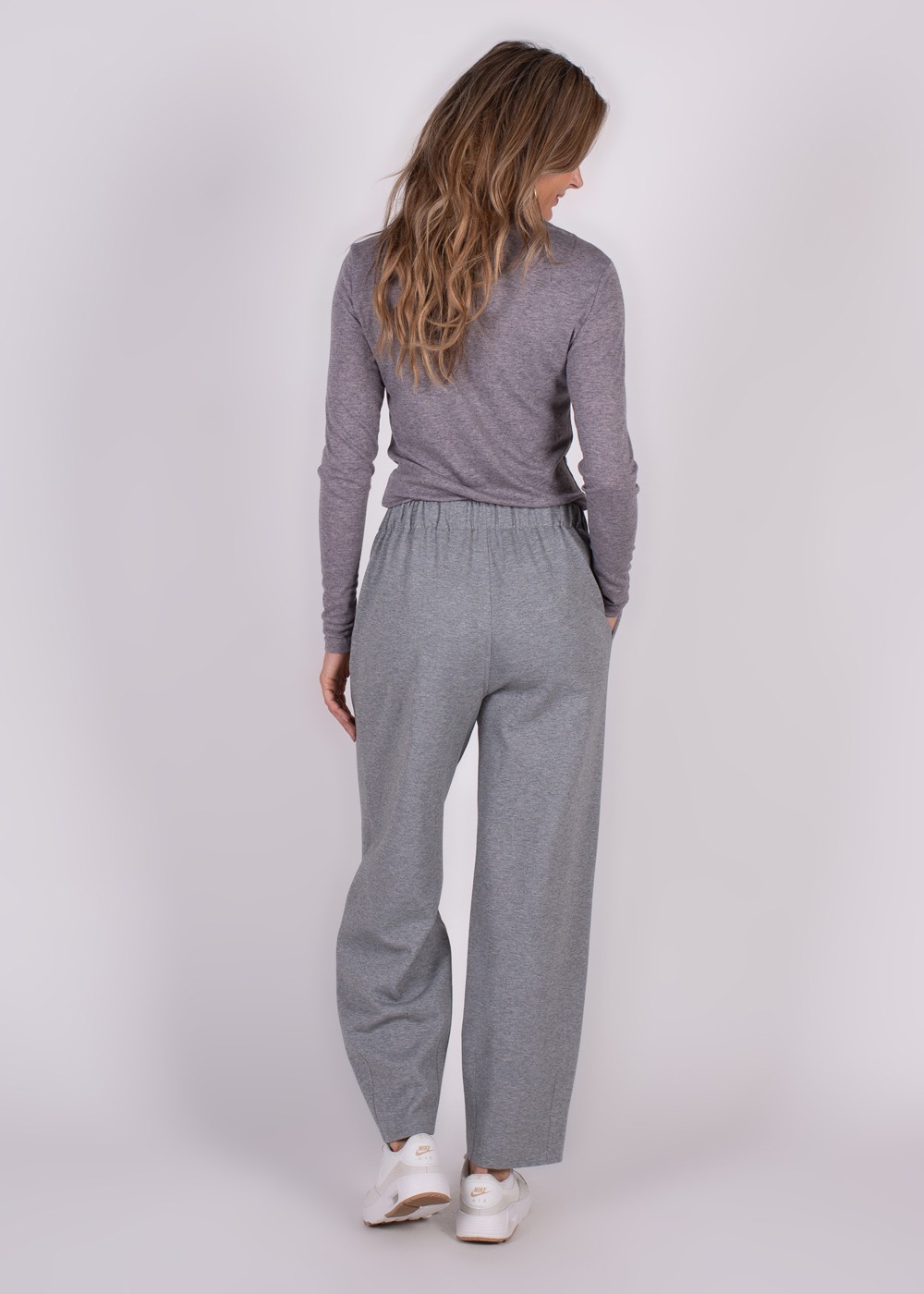 Achteraanzicht van een model dat grijze Bilbao Barrel-broek draagt met een bijpassend shirt en witte sneakers.