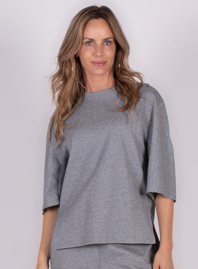 Een vrouw draagt een grijze Bilbao Sweater Malaga, gefotografeerd van voren met een neutrale achtergrond.
