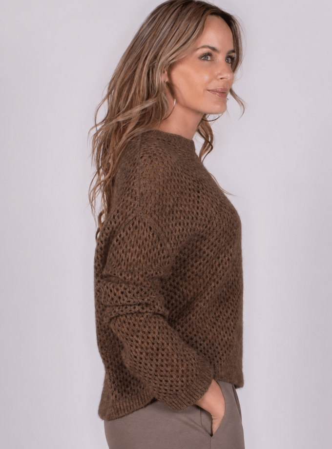 Model in warme, bruin gebreide trui en taupe broek, zijaanzicht.