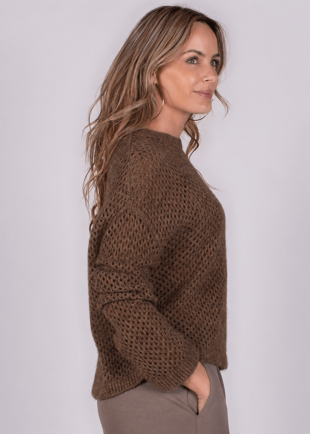 Model in warme, bruin gebreide trui en taupe broek, zijaanzicht.