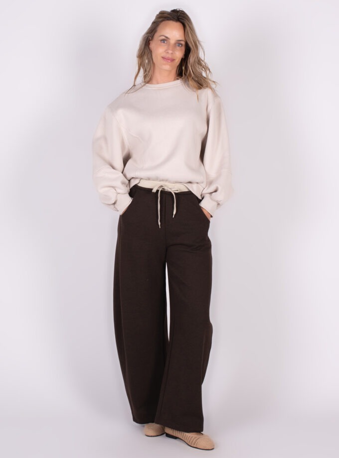 Model draagt een oversized Capri sweater in crème met bruine wijde broek en beige schoenen tegen een witte achtergrond.