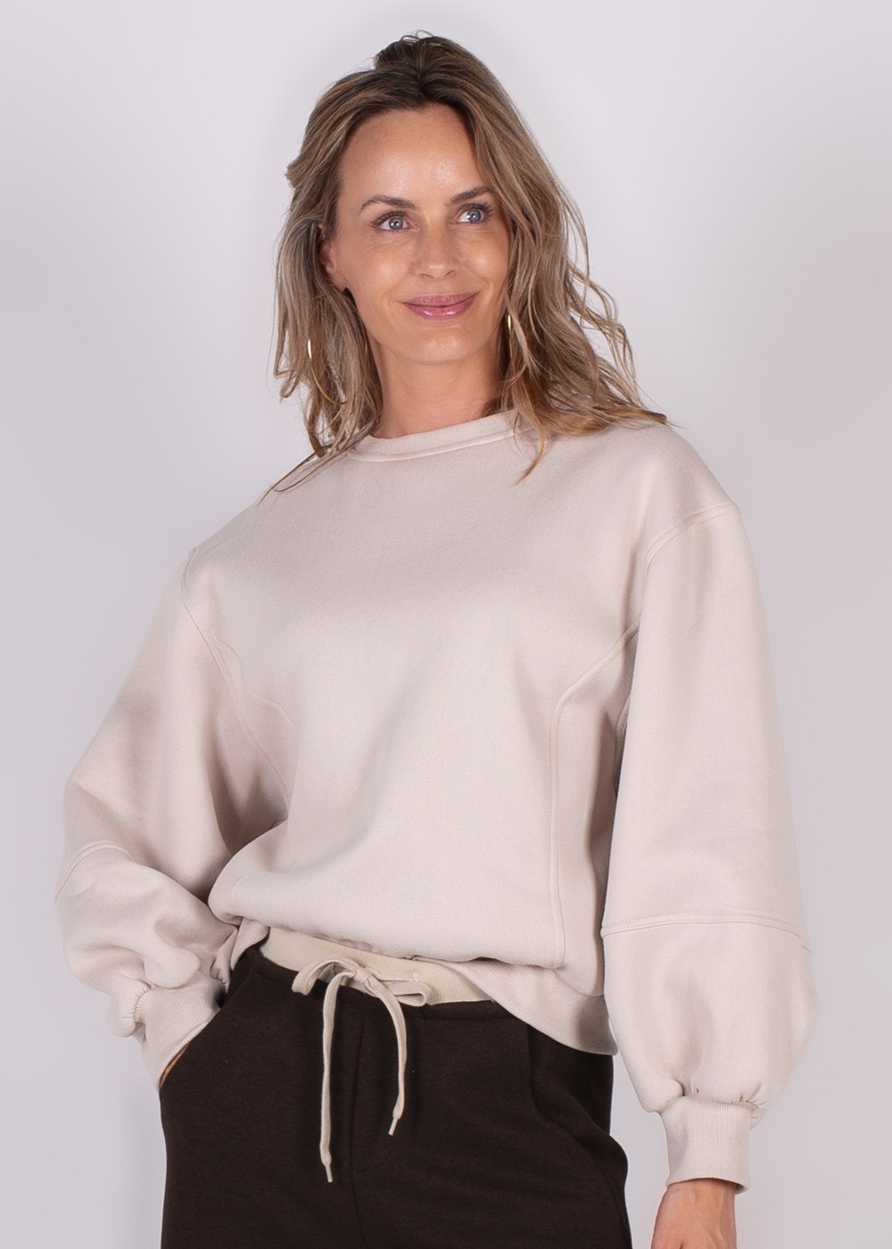 Een vrouw poseert in een crèmekleurige, oversized Capri sweater met lange mouwen en een ronde hals.