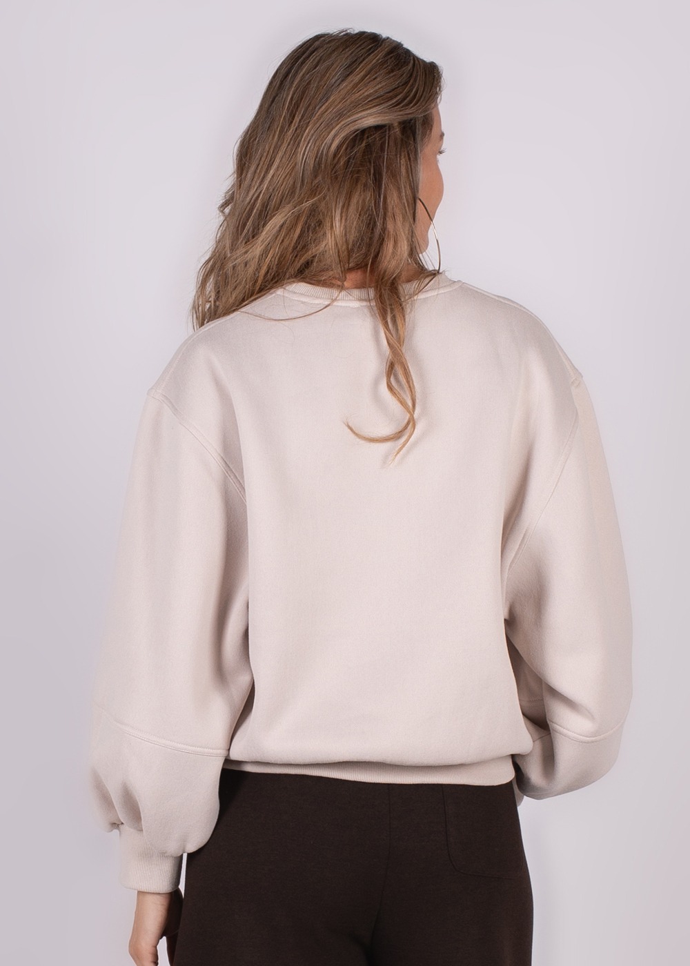 Achteraanzicht van een vrouw die een beige, oversized "Capri" sweater draagt met haar los hangend over de schouders.