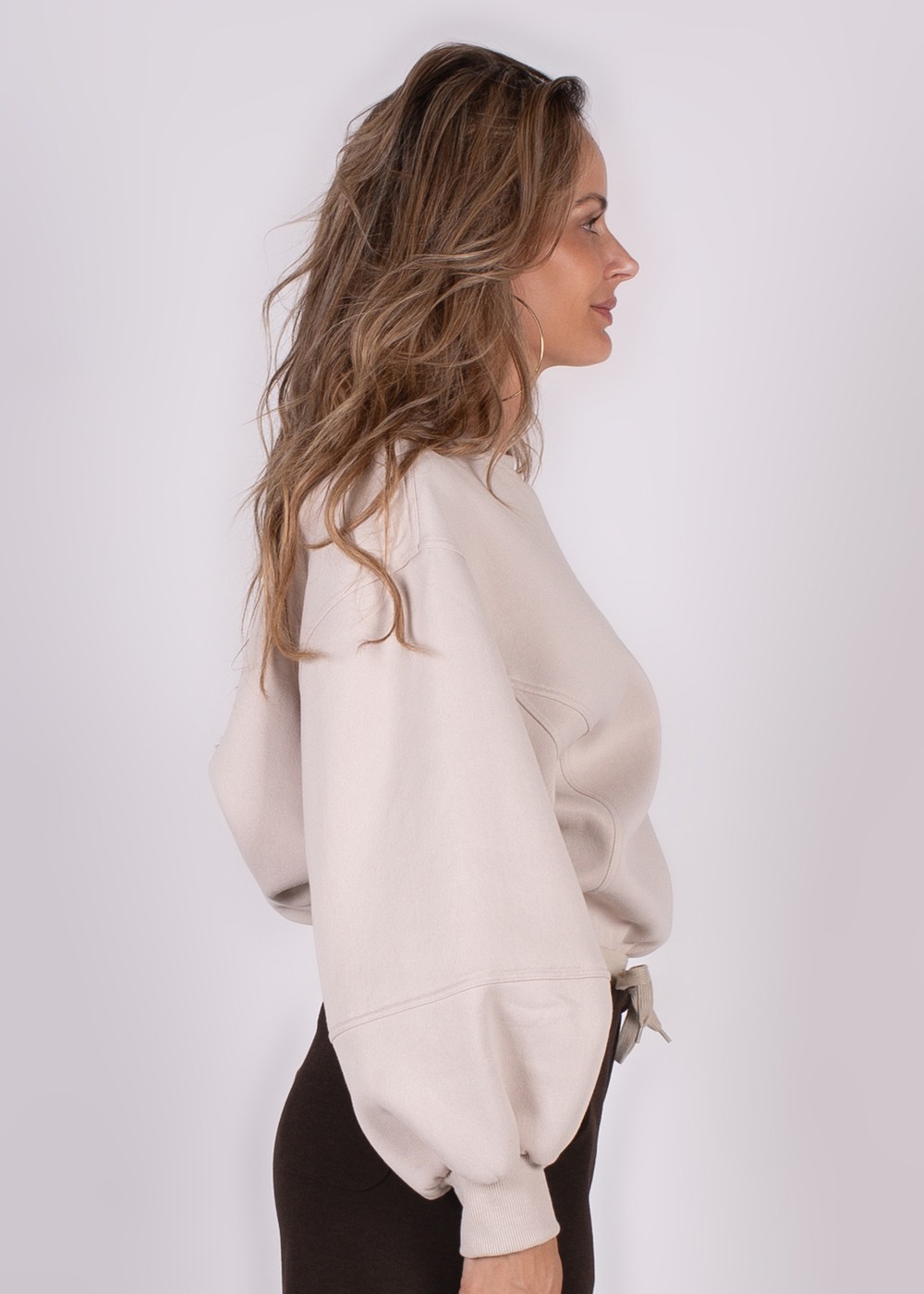 Model draagt een oversized Capri sweater in een zijaanzicht, met haar tot op de schouder in een lichte ruimte.