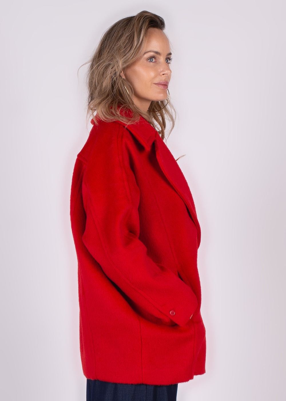 Zijaanzicht van een vrouw die een rode jas genaamd "Depok coat-55" draagt tegen een lichte achtergrond.