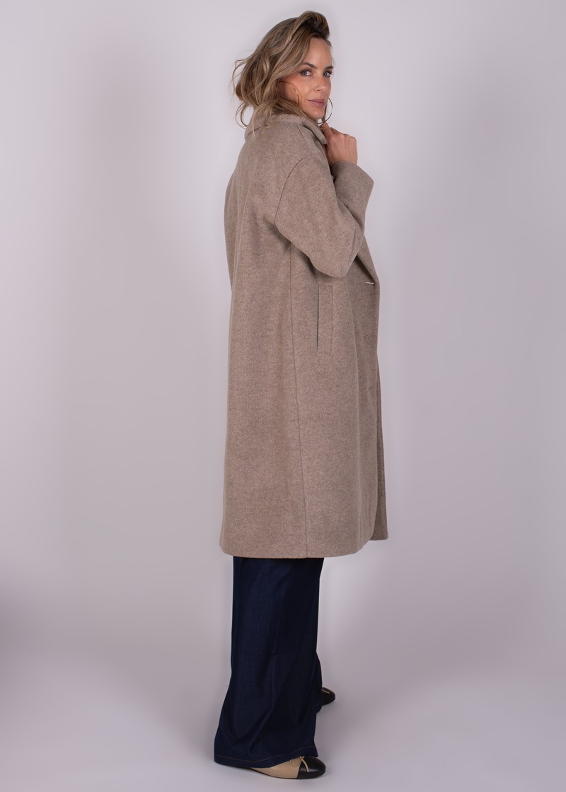 Een vrouw draagt een lange, beige jas genaamd "Depok long coa-227" terwijl ze in profiel richting de camera kijkt.