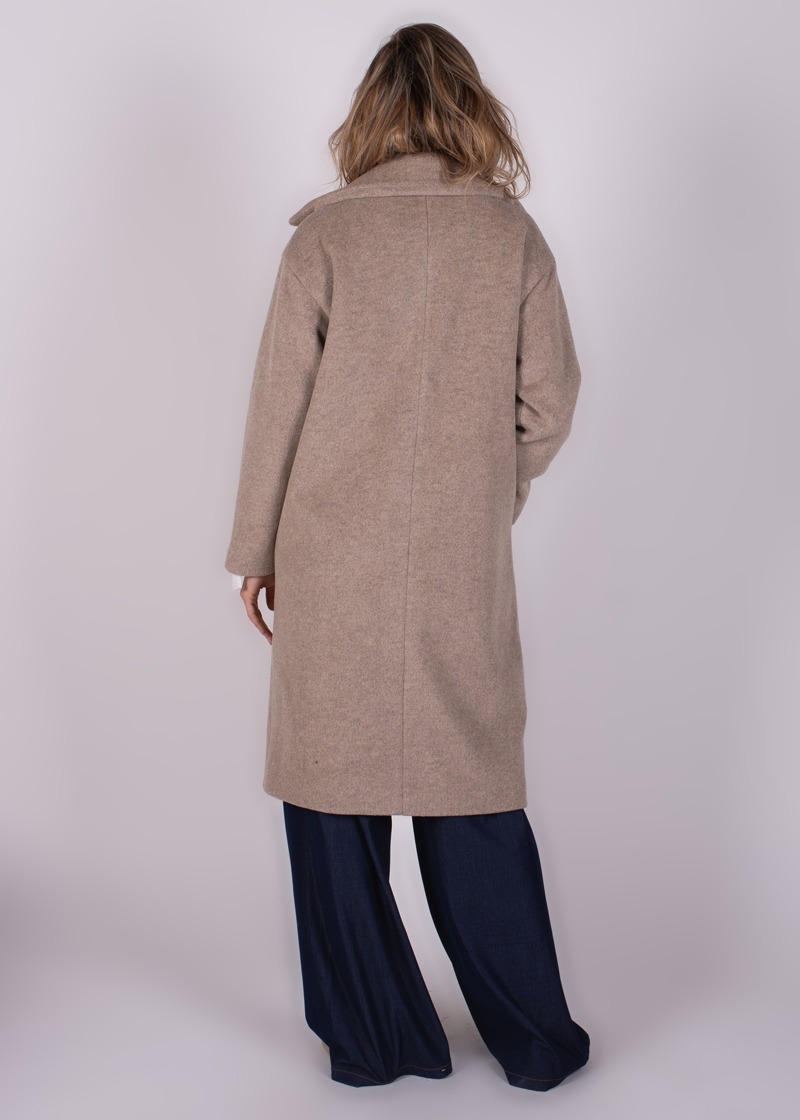Een model draagt een beige lange jas, bekend als "Depok long coat-231", van achteren gezien over een donkerblauwe broek.