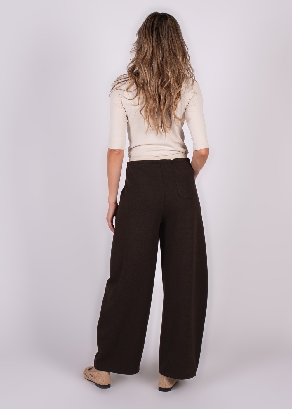 Een model, gezien van achteren, draagt een donkerbruine Helsinki pantalon en een beige top.
