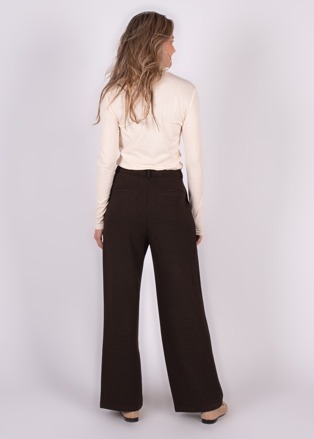 Model draagt Helsinki piran broek in bruin, gezien vanaf de achterkant, gecombineerd met een crèmekleurige top.