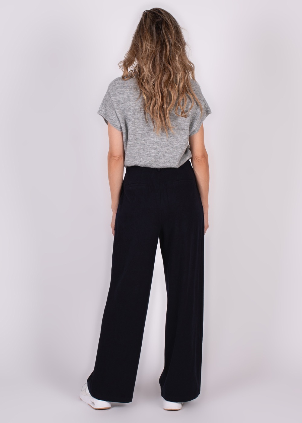 Model draagt zwarte wijde broek met grijs T-shirt, vanuit achterkant gezien.