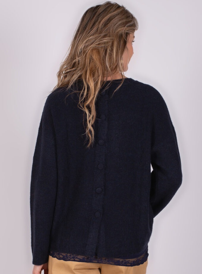 Een vrouw met los blond haar, draagt een navykleurige Lamia cardigan met knopen op de rug, gezien vanuit een achteraanzicht.