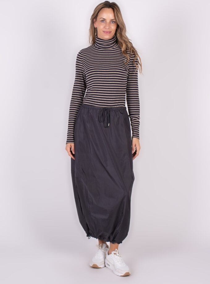 Een vrouw draagt een zwarte "Lubia" rok met koord en een gestreepte coltrui, gefotografeerd op een neutrale achtergrond.