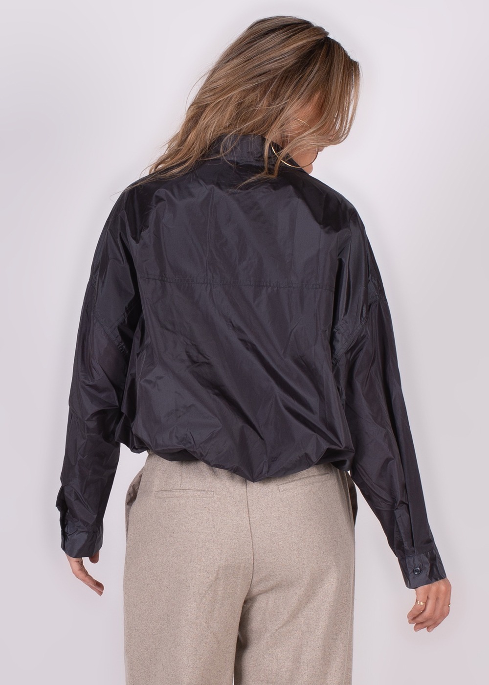 Een persoon gefotografeerd van achteren draagt een zwarte Lubia blouse en beige broek.