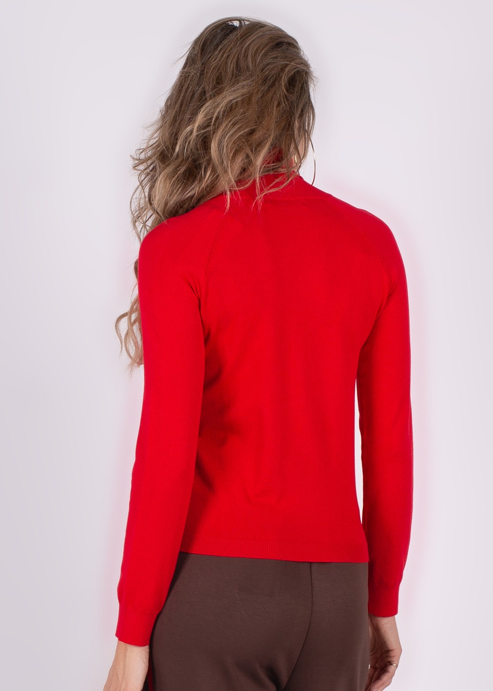 Model draagt een rode coltrui terwijl ze met haar rug naar de camera staat.