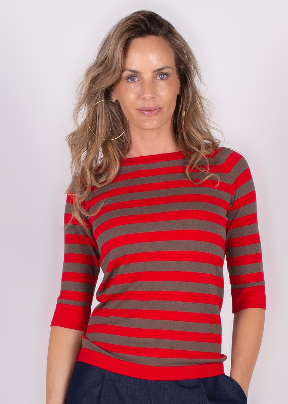 Een vrouw draagt een rood en grijs gestreepte top met driekwartsmouwen en grote hoepeloorbellen, gefotografeerd vanaf de voorkant.