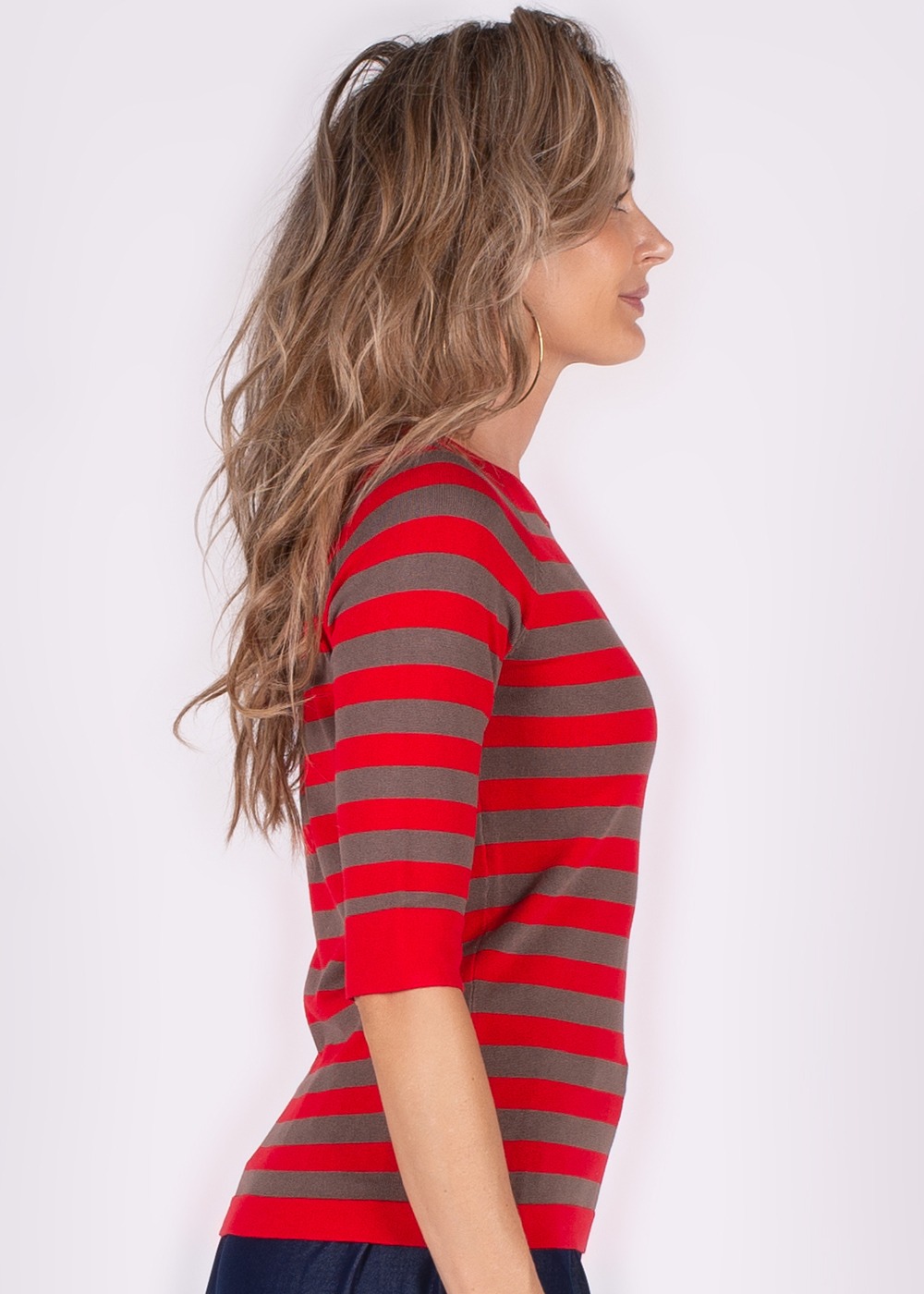 Model in zijaanzicht draagt een rood en bruin gestreepte trui met driekwart mouwen.