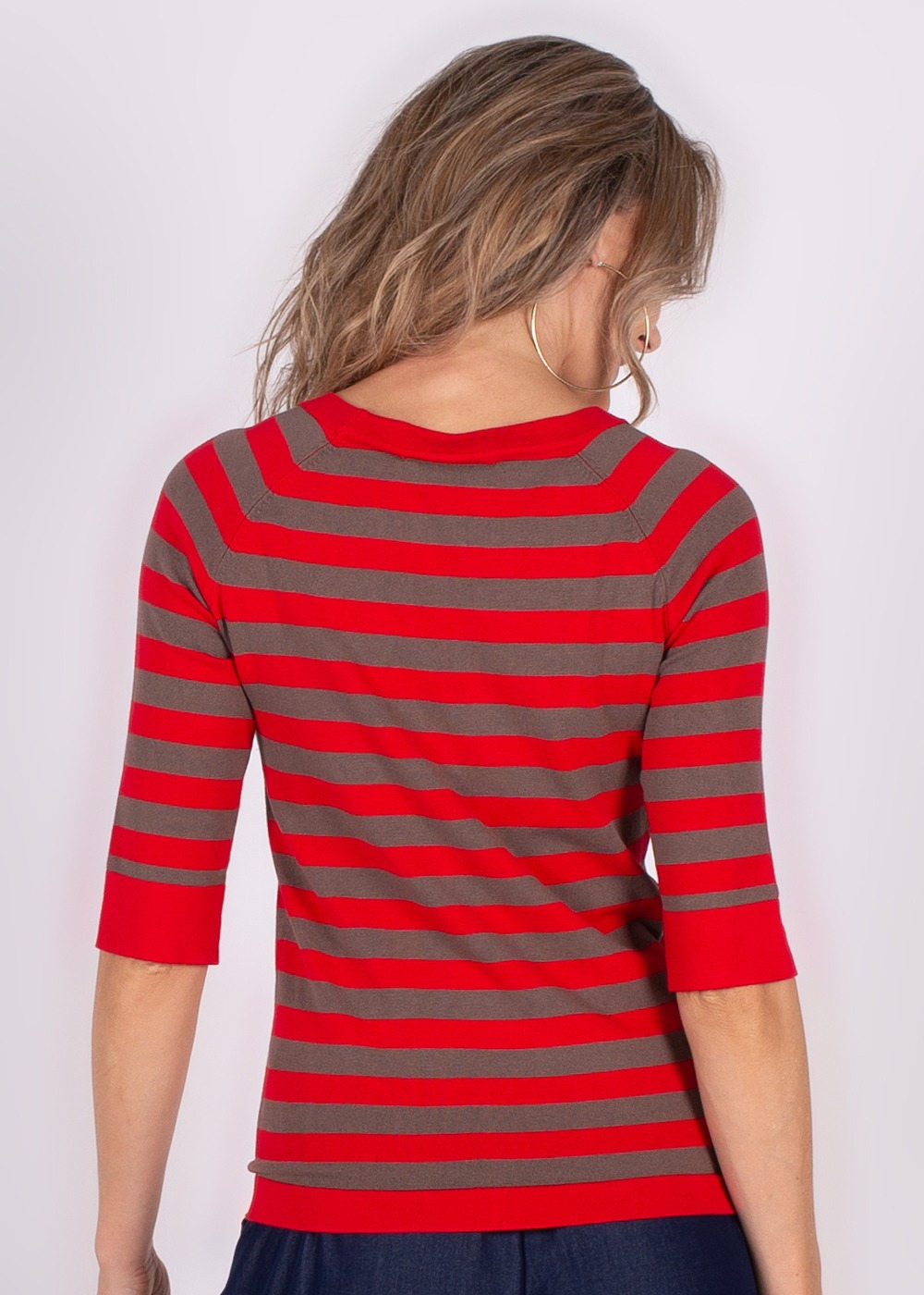Model van achteren met lang haar draagt een gestreepte rood-grijze trui met driekwart mouwen.
